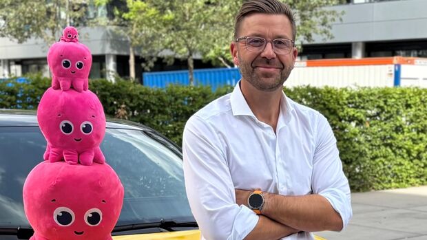 Achim Hirsch von Octopus Electric Vehicles vor einem gelben Elektroauto mit den pinken Octopus-Maskottchen.