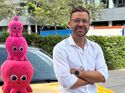 Achim Hirsch von Octopus Electric Vehicles vor einem gelben Elektroauto mit den pinken Octopus-Maskottchen.