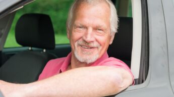 Älterer Mann mit grauem Bart lehnt lächelnd aus dem Autofenster – Symbolbild für Aktivrentner mit Dienstwagen