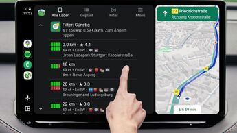 Android Auto Display zeigt Charging Time Ladeplanung mit Preisvergleich und Kartenroute, Hand tippt auf Ladesaeulenliste.