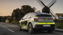 Audi A2 E-Tron Prototyp mit Tarnbeklebung während der Fahrt aus Heckperspektive vor einer Windmühle.