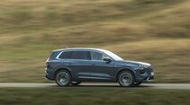 Audi Q7 in Seitenansicht während der Fahrt auf einer Landstraße vor einer durch Bewegungsunschärfe geprägten Landschaft.