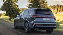 Audi Q7 während der Fahrt schräg von hinten auf einer Landstraße mit beleuchteten Rückleuchten und Audi-Ringen.