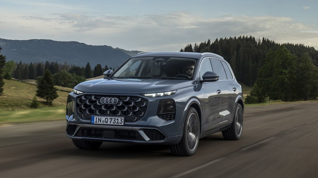 Audi Q7 während der Fahrt schräg von vorn auf einer Landstraße mit Wald und Bergen im Hintergrund.