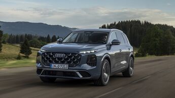Audi Q7 während der Fahrt schräg von vorn auf einer Landstraße mit Wald und Bergen im Hintergrund.