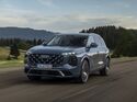 Audi Q7 während der Fahrt schräg von vorn auf einer Landstraße mit Wald und Bergen im Hintergrund.