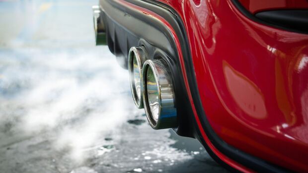 Auspuff eines Fahrzeugs mit sichtbaren Abgasemissionen in einer Werkstattumgebung