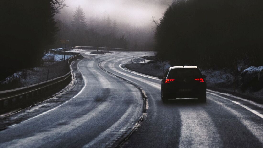 Auto fährt auf einer kurvigen Landstraße bei winterlichen Bedingungen und eingeschränkter Sicht durch eine bewaldete Landschaft