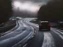 Auto fährt auf einer kurvigen Landstraße bei winterlichen Bedingungen und eingeschränkter Sicht durch eine bewaldete Landschaft