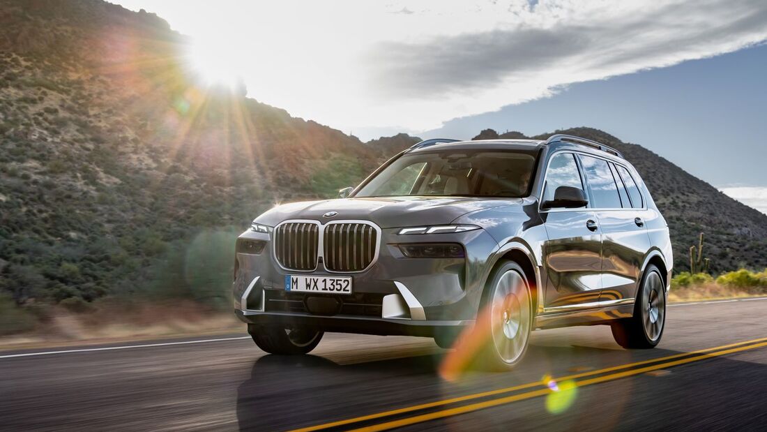 BMW X7 SUV in grauer Lackierung bei einer Fahrt auf einer Landstraße mit Berglandschaft im Hintergrund.