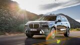 BMW X7 SUV in grauer Lackierung bei einer Fahrt auf einer Landstraße mit Berglandschaft im Hintergrund.