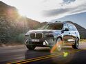 BMW X7 SUV in grauer Lackierung bei einer Fahrt auf einer Landstraße mit Berglandschaft im Hintergrund.