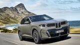 BMW iX xDrive60 in Frontansicht während der Fahrt auf einer Küstenstraße vor Berg- und Meereskulisse.