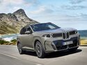BMW iX xDrive60 in Frontansicht während der Fahrt auf einer Küstenstraße vor Berg- und Meereskulisse.