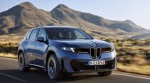 BMW iX3 Elektro-SUV in blauer Lackierung während der Fahrt auf einer Landstraße vor einer Berglandschaft.
