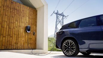BMW iX3 an bidirektionign er angeschlossen Wallbox mit Stromnetz im Hintergrund, dargestellt als Beispiel für bidirektionales Laden und Vehicle-to-Grid.