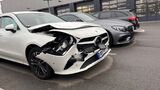 Beschädigter Mercedes mit Frontschaden auf einem Parkplatz vor einer Werkstatt.