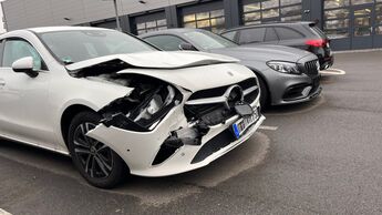 Beschädigter Mercedes mit Frontschaden auf einem Parkplatz vor einer Werkstatt.