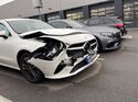 Beschädigter Mercedes mit Frontschaden auf einem Parkplatz vor einer Werkstatt.