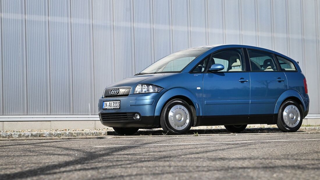 Blauer Audi A2 in schräger Front- und Seitenansicht vor einer hellen Industriehalle.