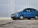 Blauer Audi A2 in schräger Front- und Seitenansicht vor einer hellen Industriehalle.
