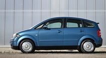 Blauer Audi A2 in vollständiger Seitenansicht vor einer hellen Industriehalle.