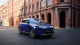 Blauer BYD Atto 3 Evo Excellence fährt auf einer Straße vor Backsteingebäuden in der Stadt.