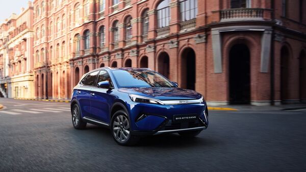 Blauer BYD Atto 3 Evo Excellence fährt auf einer Straße vor Backsteingebäuden in der Stadt.