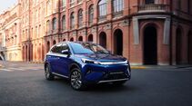 Blauer BYD Atto 3 Evo Excellence fährt auf einer Straße vor Backsteingebäuden in der Stadt.