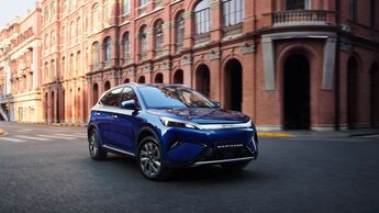 Blauer BYD Atto 3 Evo Excellence fährt auf einer Straße vor Backsteingebäuden in der Stadt.