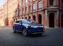 Blauer BYD Atto 3 Evo Excellence fährt auf einer Straße vor Backsteingebäuden in der Stadt.