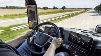 Blick aus dem Cockpit eines Mercedes-Lkw auf Straße, Display und digitale Spiegelanzeige während der Fahrt.