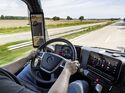 Blick aus dem Cockpit eines Mercedes-Lkw auf Straße, Display und digitale Spiegelanzeige während der Fahrt.