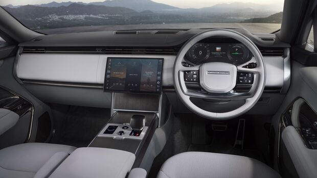 Cockpit des Range Rover Electric mit Lenkrad, digitalem Kombiinstrument, zentralem Touchscreen und heller Innenausstattung.