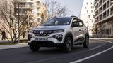 Dacia Spring Elektroauto fährt auf Straße in der Stadt zwischen Wohngebäuden.