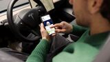 Dienstwagen-Fahrer nutzt Smartphone mit Driver App für E-Auto-Flotte im Elektroauto und sieht Fahrzeugdaten wie Ladezustand und Reichweite.