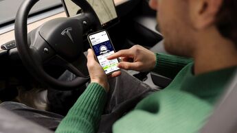 Dienstwagen-Fahrer nutzt Smartphone mit Driver App für E-Auto-Flotte im Elektroauto und sieht Fahrzeugdaten wie Ladezustand und Reichweite.