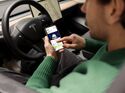 Dienstwagen-Fahrer nutzt Smartphone mit Driver App für E-Auto-Flotte im Elektroauto und sieht Fahrzeugdaten wie Ladezustand und Reichweite.