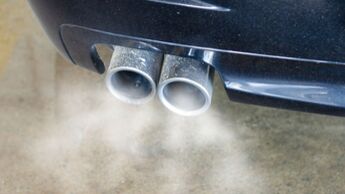 Doppelter Auspuff mit sichtbarem Abgasausstoss eines dunklen Verbrenner-Fahrzeugs – Symbolbild für CO2-Ausstoss bei Dienstwagen