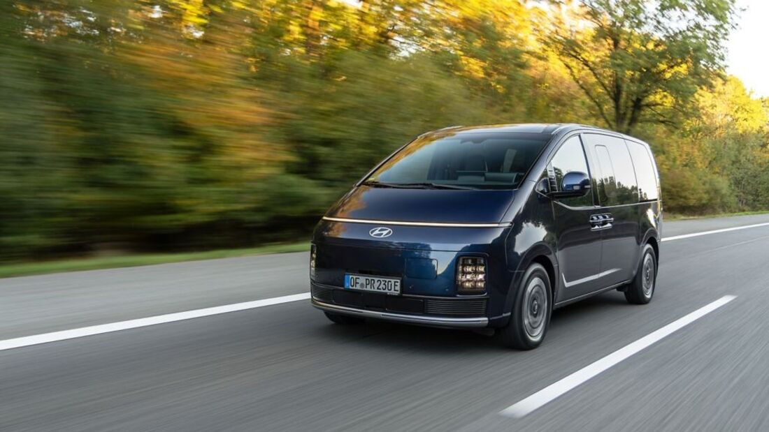 Dunkelblauer Hyundai Staria Elektro in Fahrt aus schräger Frontperspektive mit schmalem Lichtband und vertikalen Scheinwerfern.