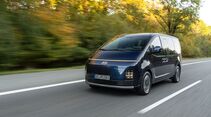 Dunkelblauer Hyundai Staria Elektro in Fahrt aus schräger Frontperspektive mit schmalem Lichtband und vertikalen Scheinwerfern.