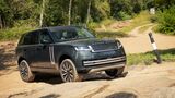 Dunkelgrüner Range Rover fährt über einen felsigen Abschnitt einer unbefestigten Strecke in bewaldetem Gelände.