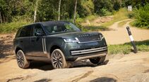 Dunkelgrüner Range Rover fährt über einen felsigen Abschnitt einer unbefestigten Strecke in bewaldetem Gelände.