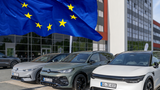 EU-Flagge vor geparkten Elektroautos an einem Unternehmensstandort.