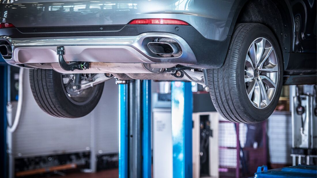Ein Pkw steht auf einer Hebebühne in einer Werkstatt, sichtbar ist der Unterboden des Fahrzeugs während einer technischen Überprüfung.
