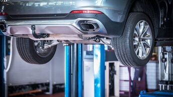 Ein Pkw steht auf einer Hebebühne in einer Werkstatt, sichtbar ist der Unterboden des Fahrzeugs während einer technischen Überprüfung.