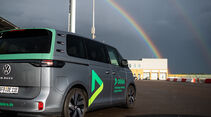 Ein VW ID. Buzz mit DEKRA-Beschriftung steht auf dem Testgelände des Lausitzrings, im Hintergrund ein heller Doppelregenbogen.