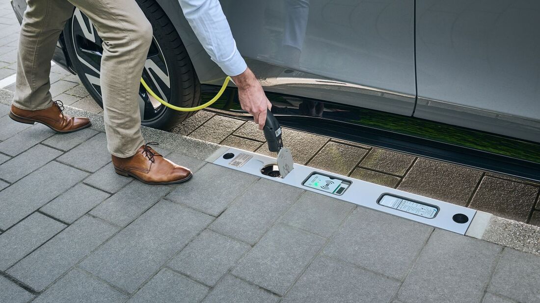 Eine Person lädt ein Elektroauto über einen im Bordstein integrierten Ladepunkt am Fahrbahnrand.