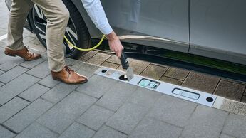 Eine Person lädt ein Elektroauto über einen im Bordstein integrierten Ladepunkt am Fahrbahnrand.