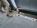 Eine Person lädt ein Elektroauto über einen im Bordstein integrierten Ladepunkt am Fahrbahnrand.